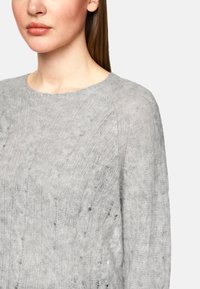 Hellgrauer Strickpullover mit lockerer Passform, rundem Halsausschnitt und strukturiertem Muster mit kleinen Löchern. Weiches, leicht durchsichtiges Material.