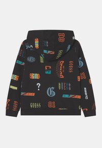 Felpa nera con loghi e numeri 'GUESS' colorati in vari caratteri e dimensioni, dotata di tasca frontale e cappuccio con cordino regolabile.