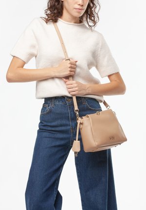 Bolso cruzado de cuero beige con forma estructurada, marca sutil y correa ajustable. Combinado con un suéter ligero y jeans de tiro alto.