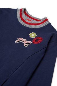 Marinegenser med en grå og rød stripet ribbestrikket krage, med broderte lapper av blomster og en sløyfe i rosa, grønt og rødt.