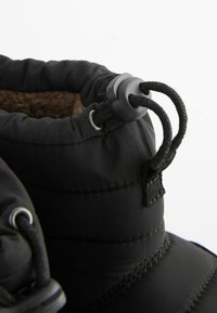 Bottes d'hiver noires avec un upper rembourré, un cordon de serrage ajustable, des œillets en métal et un intérieur texturé. La semelle est plate et durable.