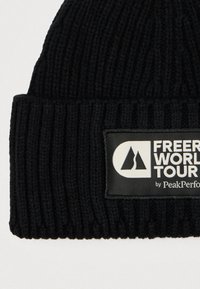 Black knitted beanie features a ribbed texture and a rectangular label with "Freeride World Tour by PeakPerformance" in white and black.