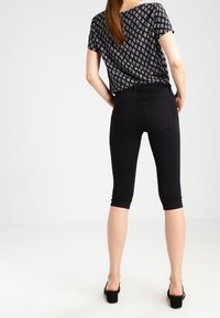 Pantalones capri negros con un diseño ajustado, que presentan una textura suave y bolsillos traseros visibles, combinados con una blusa negra con estampado.