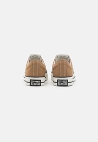 Sneaker Converse All Star in tela marrone con cuciture bianche, suole in gomma nera e branding classico sul tallone. Design a profilo basso.