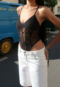 Zwarte kanten bodysuit met dunne bandjes, met ingewikkelde bloemenpatronen, gecombineerd met hoge witte denim shorts.