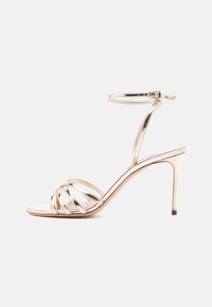 Zlatá kovová sandála na vysokom podpätku s viacerými tenkými pásikmi cez prsty a remienkom okolo členka so zapínaním na sponu.