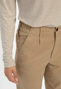 Beige Baumwoll-Chinos mit geradem Bein, ausgestattet mit Seitentaschen, einem Knopfverschluss und dezenten Nähten.