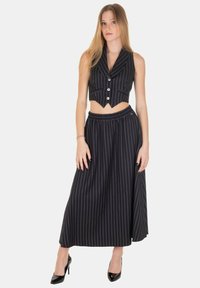 Completo a due pezzi nero a righe sottili con gilet cropped con bottoni e gonna lunga con fascia elastica in vita. Décolleté nere lucide.