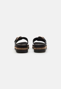 Sorte sandaler med en korklignende såle, med justerbar stropp og glatt overflate. Bakfra viser bildet stroppen og den polstrede sålen.