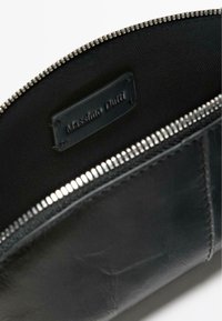 Sort læderpung med tekstureret finish, der har lynlåslukning og en lille mærket label indvendigt. Indersiden er lavet af et kontrasterende stof.