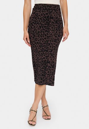 Femme portant une jupe crayon midi marron à imprimé léopard noir, associée à des sandales à talons hauts noires à lanières et un haut blanc.