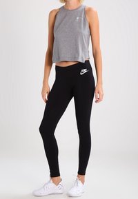 Grå kortärmad topp med rund halsringning, kombinerad med svarta leggings som har en vit Nike-logga. Vita snörskor i sportmodell fulländar outfiten.