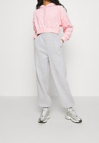 Rosa cropped Hoodie mit strukturiertem Muster, Kordelzug und elastischem Saum, kombiniert mit hellgrauen Sweatpants mit weitem Bein und silbernen Sneakern.