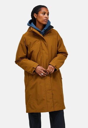 Bruine waterdichte parka met een capuchon, voorzien van een ritsluiting, zijzakken en een ontspannen pasvorm. Draagt over een blauwe hoodie.