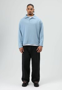 Hellblauer Pullover mit Kragen und drei Knöpfen, kombiniert mit lockeren schwarzen Jeans und schwarzen Schuhen. Glatter Stoff und entspannte Passform.