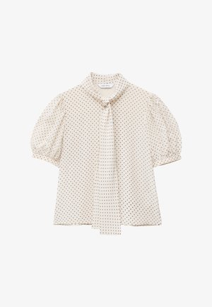 Blouse crème à petits pois, manches courtes bouffantes et détail de nouage à l'encolure devant.
