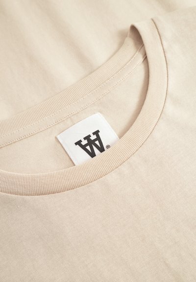 Beige Baumwoll-T-Shirt mit geripptem Rundhalsausschnitt. Verfügt über ein gewebtes Etikett mit dem Buchstaben "W" am Kragen. Weiche Textur und glatte Oberfläche.