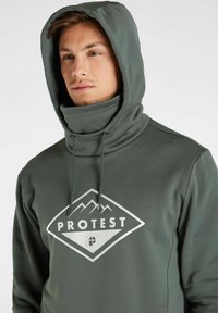 Felpa verde scuro con colletto alto e cordoncini regolabili. Presenta un grande logo bianco a forma di diamante con montagne e il testo "PROTEST."