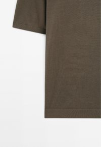 T-shirt a maniche corte di colore verde oliva scuro, realizzato in tessuto liscio con una sottile texture; presenta un bordo dritto e una vestibilità rilassata.