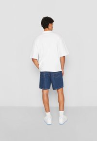 Tricou alb cu maneci scurte și pantaloni scurți din denim cu buzunare, purtat cu adidași albi și sosete vizibile până la glezne. Un look simplu și casual.