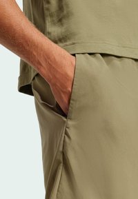 Camisa de mezcla de algodón verde olivo con un corte relajado. Diseño de mangas cortas con un detalle de bolsillo en la costura lateral. Textura suave y lisa.