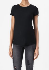 Mustat ribbattu äitiys t-paita, jossa on lyhyet, röyhelöillä varustetut hihat, pyöreä pääntie ja vartalonmyötäinen malli, yhdistettynä kulutettuihin harmaisiin skinny-farkkuihin.