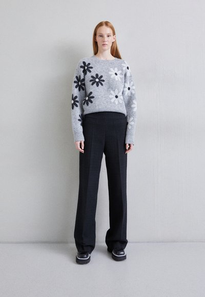 Grå strikket sweater med sort-hvide blomster mønstre, parret med sorte strukturerede bukser og sorte sko med sølv detaljer.