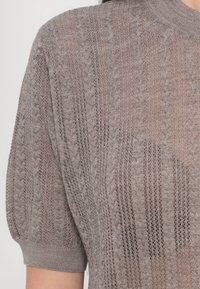 Svetlohnedý pletený sveter s textúrovaným kabelovým vzorom, krátkymi rukávmi a rebrovaným výstrihom. Priesvitná tkanina s voľným strihom.