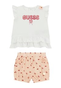 Hvid top med volangærmer, rød "GUESS love" broderi, parret med lyserøde shorts med kirsebærmønstre og dekorative lommer.