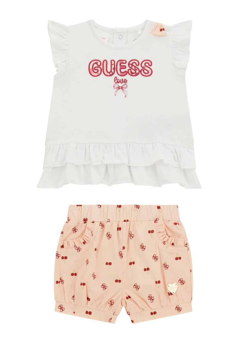 Hvid top med volangærmer, rød "GUESS love" broderi, parret med lyserøde shorts med kirsebærmønstre og dekorative lommer.