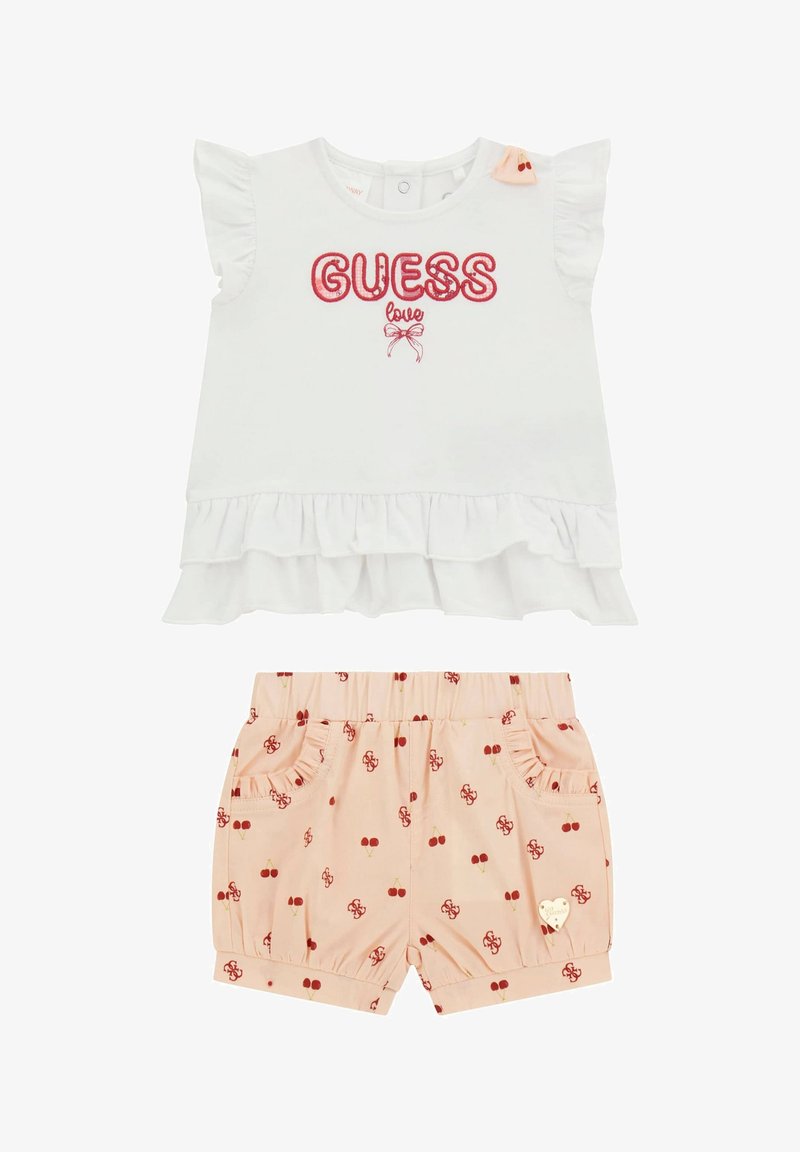 Top bianco con maniche a volant, ricamo rosso "GUESS love", abbinato a pantaloni corti rosa con motivi di ciliegie e tasche decorative.