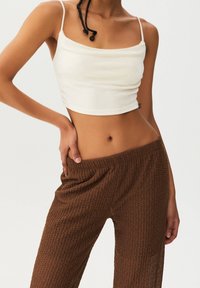 Top blanc court avec des bretelles fines, associé à un pantalon en tricot marron ample présentant un motif texturé. Les deux vêtements sont ajustés.