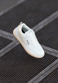 Hvit lær sneakers med perforert tå, teksturert sidepanel, gummigummisåle og en løpeflik på hælen. Fila-logoen på siden.