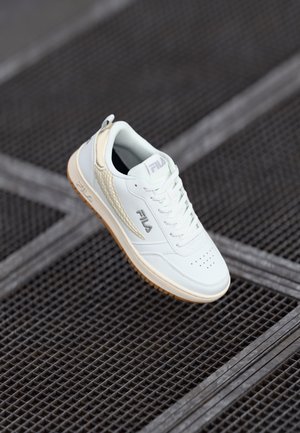 Hvit lær sneakers med perforert tå, teksturert sidepanel, gummigummisåle og en løpeflik på hælen. Fila-logoen på siden.