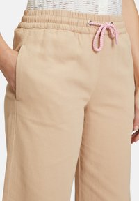 Beige katoenen broeken met een trekkoord taille, voorzien van een gevlochten roze accent. Zijkanten met zakken en een ontspannen pasvorm, gemaakt van gladde stof.