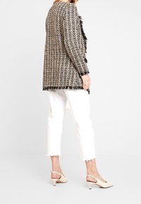 Tweedblazer i svart och beige med fransdetaljer, kombinerad med vita cropped-byxor och beige slingback-klackar med en liten klack.