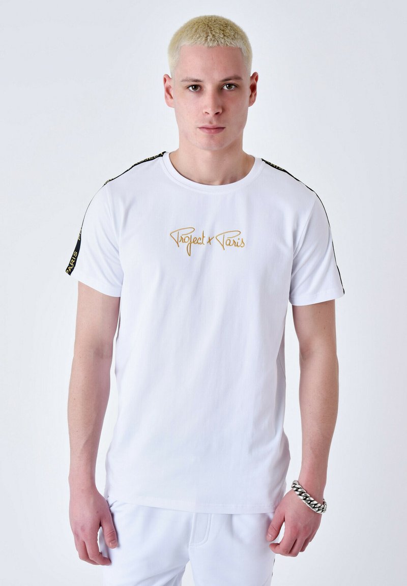 Camiseta de algodón blanca con un logo dorado de "Project Paris" en el frente, con detalles y rayas negras a lo largo de los hombros.