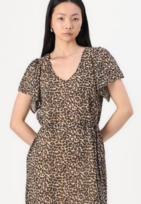 Šaty s leopardím vzorom v hnedej a béžovej farbe, s krátkymi voľne splývajúcimi rukávmi, V-výstrihom a voľným siluetou so stiahnutým pásom.