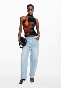 Zwart-oranje mouwloze top met gedrapeerd ontwerp, gecombineerd met lichtblauwe wijd uitlopende jeans. Model houdt een zwarte handtas vast.