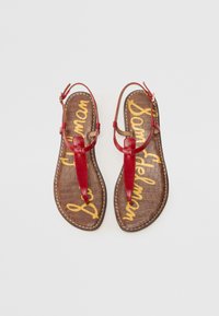 Red leather thong sandals with a textured brown insole featuring a crocodile pattern and yellow branding in a decorative script.