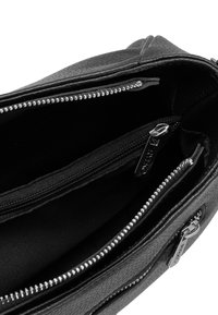 Interno di una borsa in pelle nera che mostra due tasche con zip, materiale testurizzato e rivestimento nero liscio. Sono presenti dettagli in metallo argentato.