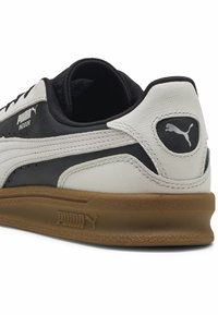 Čierno-biele tenisky s textúrovaným dizajnom, s gumovou podrážkou, prešívanými detailmi a logom Puma na päte a boku.