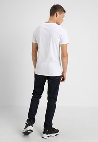 Hvid bomulds T-shirt med rund hals, der er parret med mørkeblå jeans og sorte sneakers. Glat tekstur, enkelt design og afslappet pasform.