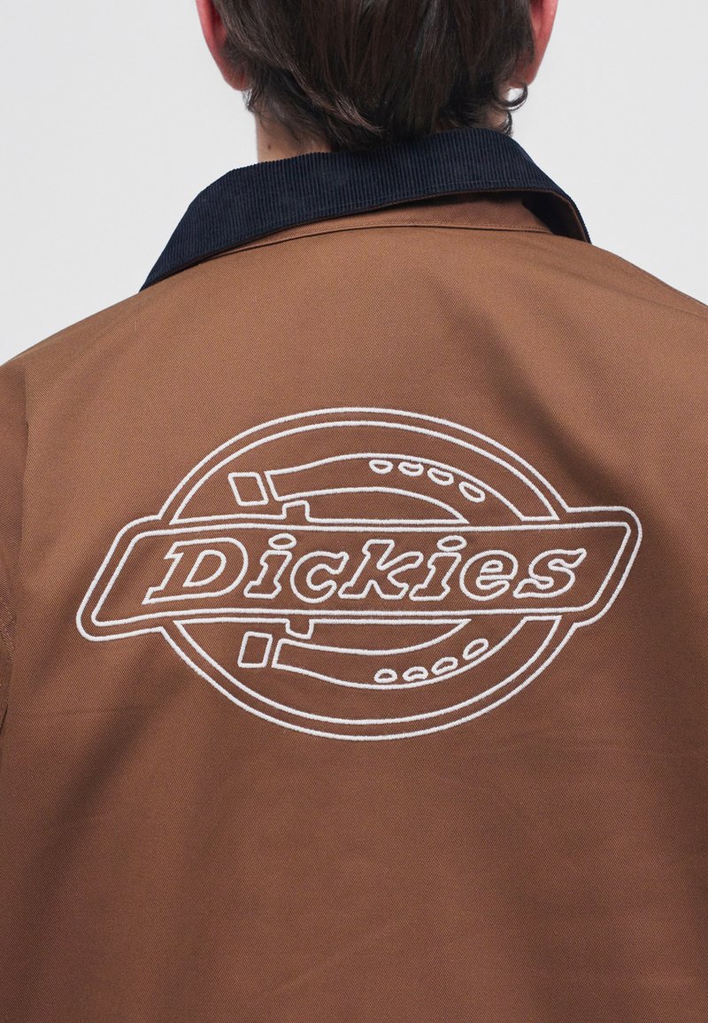 Back view of person wearing brown jacket with black collar and white outlined "Dickies" logo on the back.