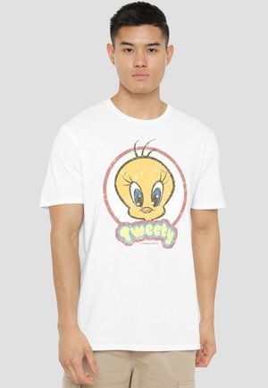 Young man wearing a white T-shirt with a large colorful Tweety Bird cartoon face and text on the front, standing against a plain background.