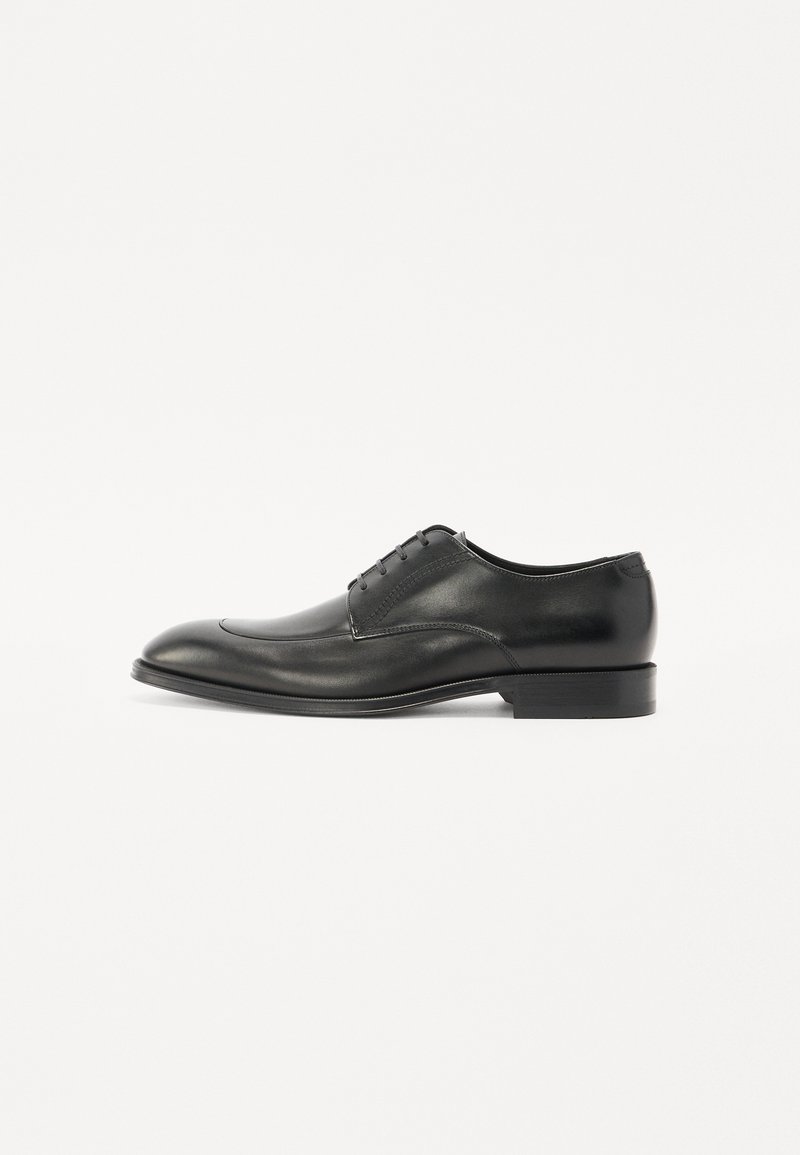 Elegante scarpa da uomo in pelle nera con finitura liscia, punta rotonda, cinque occhielli e tacco basso. Presenta cuciture sottili lungo i bordi.