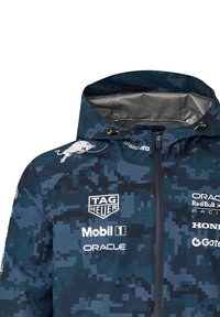 Niebieska kurtka w kamuflażu z kapturem, z logo: TAG Heuer, Oracle i innymi. Materiał ma lekkie połysku, teksturowaną powierzchnię i zamek błyskawiczny.