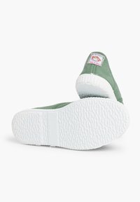 Baskets en toile vertes avec une semelle en caoutchouc blanc. Présentent une étiquette rose et blanche à l'arrière. Fond texturé pour une meilleure adhérence.