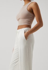 Beżowy prążkowany top typu crop w zestawieniu z białymi lnianymi spodniami z elastycznym paskiem w talii i bocznymi kieszeniami. Całość charakteryzuje się swobodnym stylem.