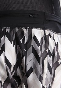 Svartvita mönstrade shorts med en geometrisk chevrondesign, med ett svart elastiskt midjeband och synliga sömnadsdetaljer.